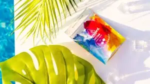 A vibrant packet of water sits beside a green leaf next to a sparkling pool, adding a splash of color to the scene.