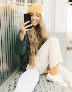 A woman sits on a bench, casually holding a skateboard beside her, enjoying a sunny day outdoors.