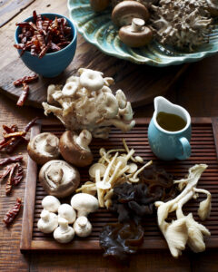 High angle view of various mushrooms on wooden board and dried chillis in bowl